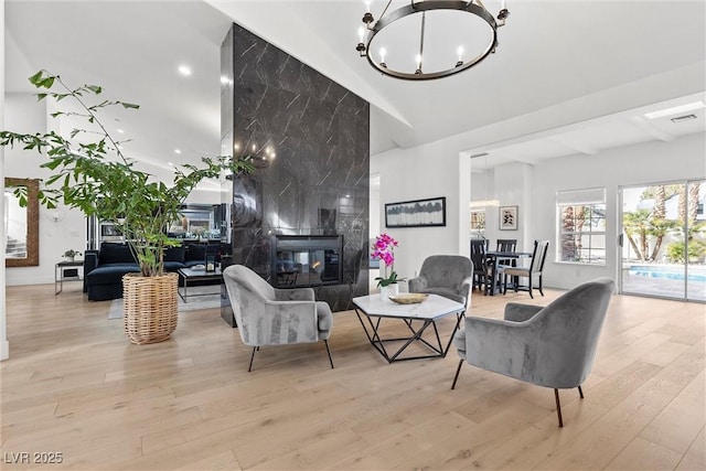 living area with visible vents, a high end fireplace, an inviting chandelier, wood finished floors, and high vaulted ceiling
