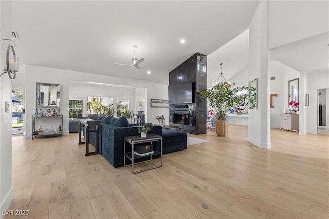 living room featuring baseboards, light wood-type flooring, a large fireplace, and high vaulted ceiling