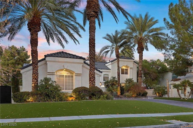 view of front of house with stucco siding, a tiled roof, and a yard