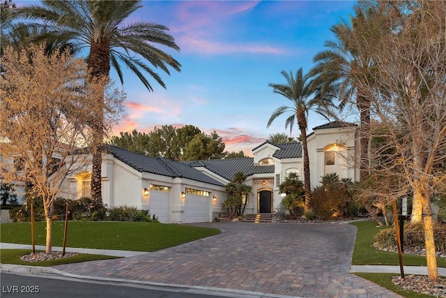 mediterranean / spanish home with stucco siding, decorative driveway, a tile roof, a front yard, and an attached garage