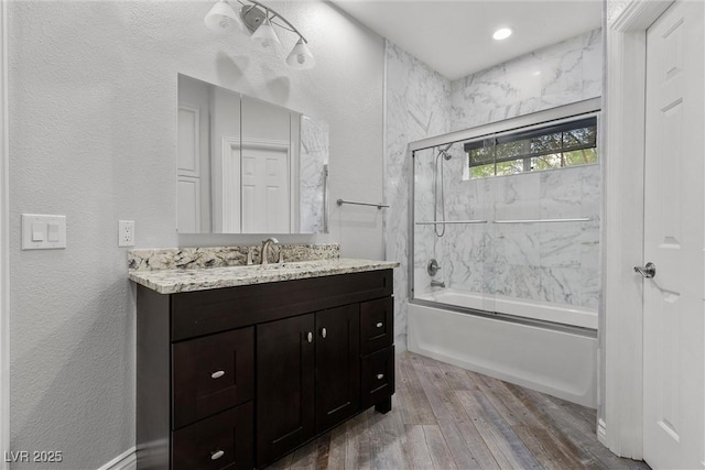 full bath with shower / bath combination with glass door, vanity, a textured wall, and wood finished floors