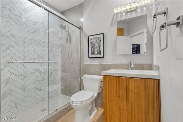 full bath featuring tile walls, vanity, toilet, a stall shower, and wainscoting