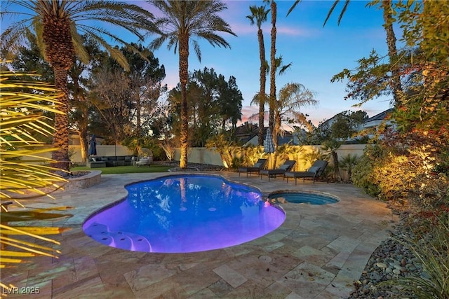 pool at dusk with a pool with connected hot tub, a patio, and a fenced backyard