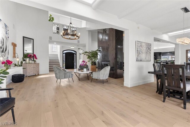 living room featuring stairs, a notable chandelier, a high ceiling, and light wood-style flooring