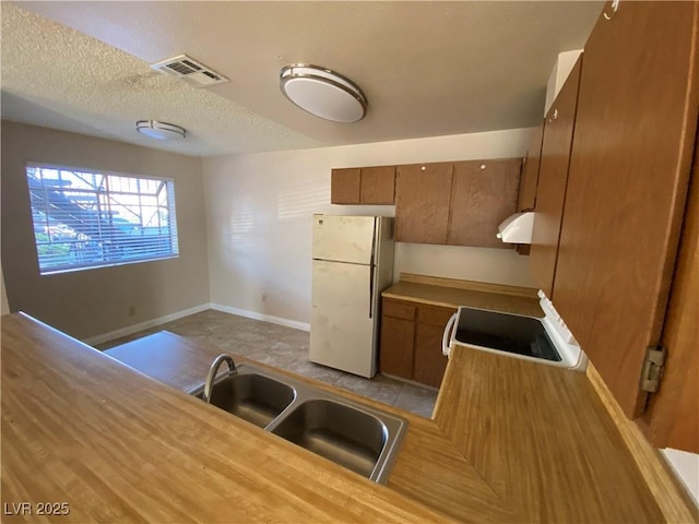 2685 Bryandouglas Dr, Las Vegas, NV 89121 - kitchen with freestanding refrigerator, brown cabinets, range, a sink, and a textured ceiling