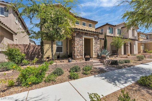 mediterranean / spanish house with a tile roof, a residential view, fence, stone siding, and stucco siding