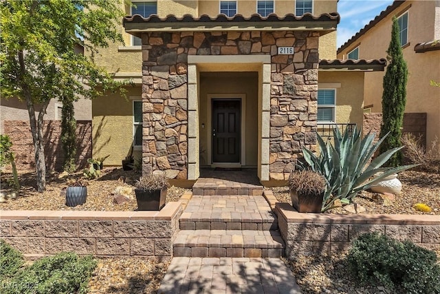 doorway to property featuring a tiled roof, stone siding, and stucco siding