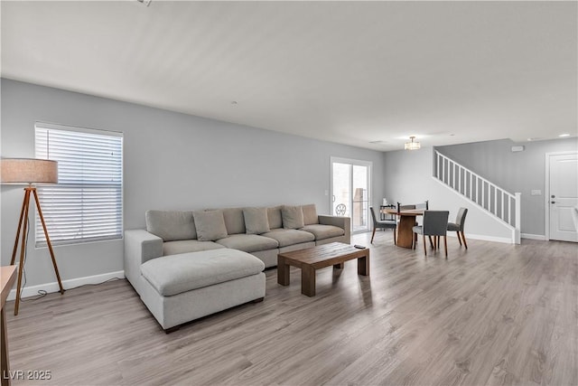 living area featuring baseboards, light wood-style flooring, and stairway