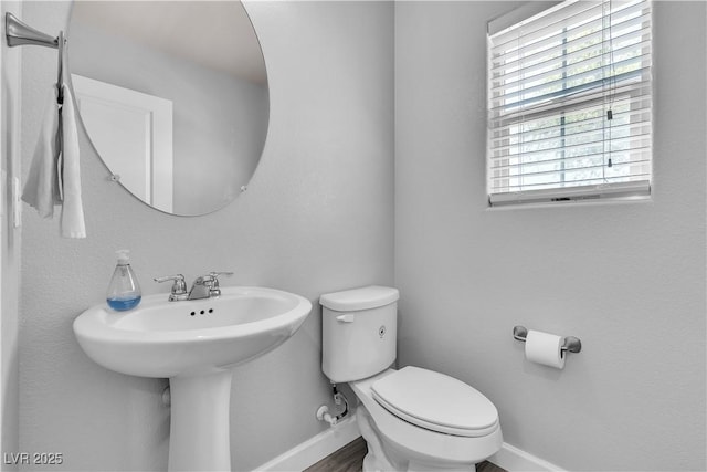 half bathroom featuring baseboards, a sink, wood finished floors, and toilet