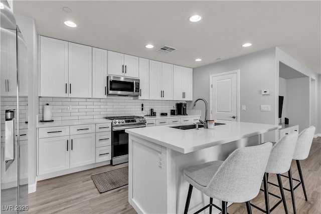 kitchen featuring appliances with stainless steel finishes, a sink, a kitchen bar, backsplash, and visible vents