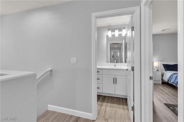 ensuite bathroom featuring vanity, ensuite bath, baseboards, wood finished floors, and visible vents
