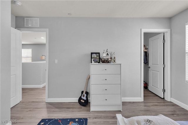 bedroom with baseboards, a walk in closet, wood finished floors, and visible vents