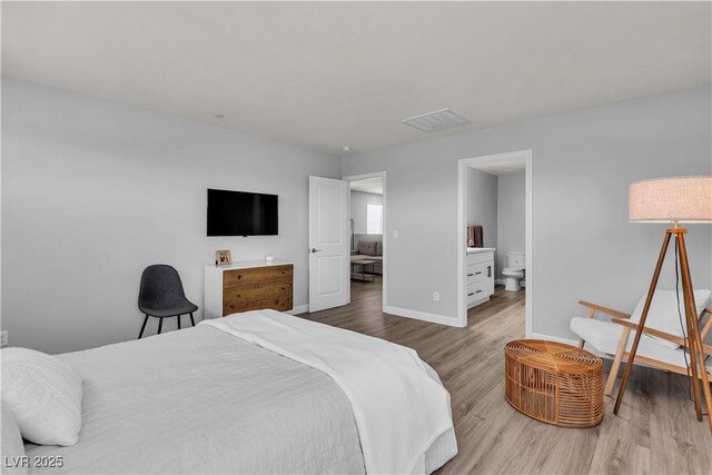 bedroom featuring baseboards, ensuite bath, wood finished floors, and visible vents