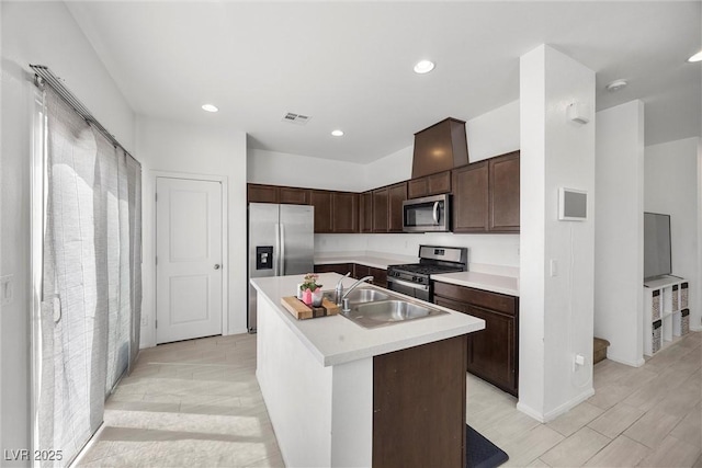 kitchen with dark brown cabinetry, a kitchen island with sink, a sink, light countertops, and stainless steel appliances