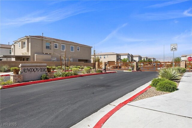 view of street featuring curbs, traffic signs, sidewalks, a gated entry, and a residential view