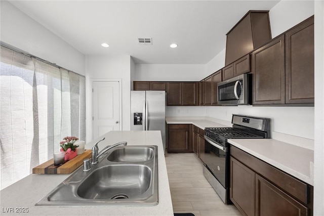 kitchen featuring dark brown cabinetry, a sink, light countertops, stainless steel appliances, and light wood-type flooring