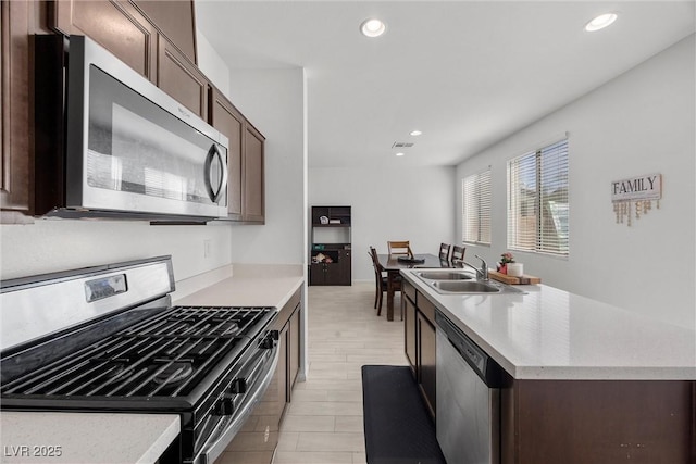 kitchen with a sink, appliances with stainless steel finishes, a kitchen island with sink, and dark brown cabinetry