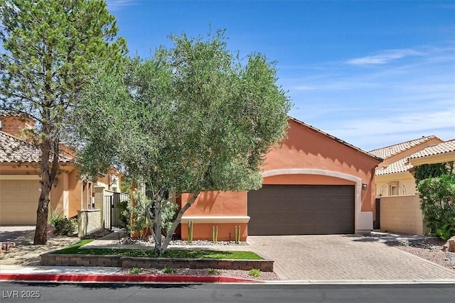 mediterranean / spanish-style house featuring stucco siding, a gate, driveway, a tiled roof, and an attached garage