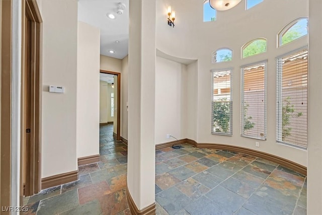 empty room featuring stone tile flooring, a healthy amount of sunlight, and baseboards
