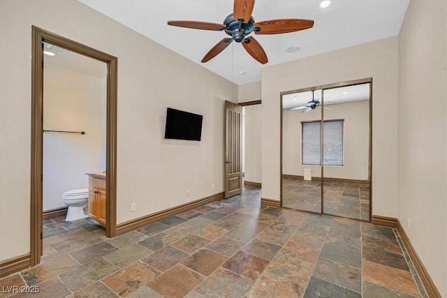 unfurnished bedroom featuring stone tile flooring, a closet, ensuite bath, and baseboards