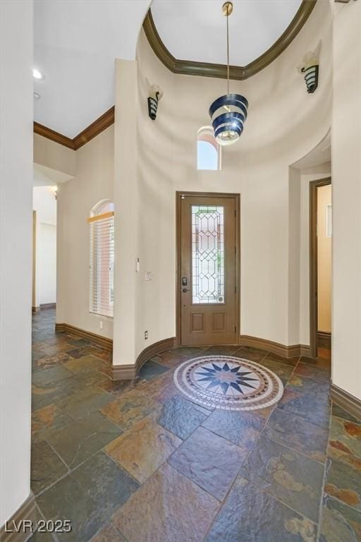 foyer featuring crown molding, a high ceiling, stone tile flooring, and baseboards