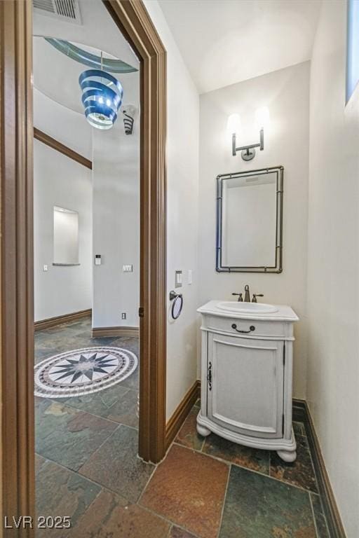 bathroom with visible vents, stone tile floors, vanity, and baseboards