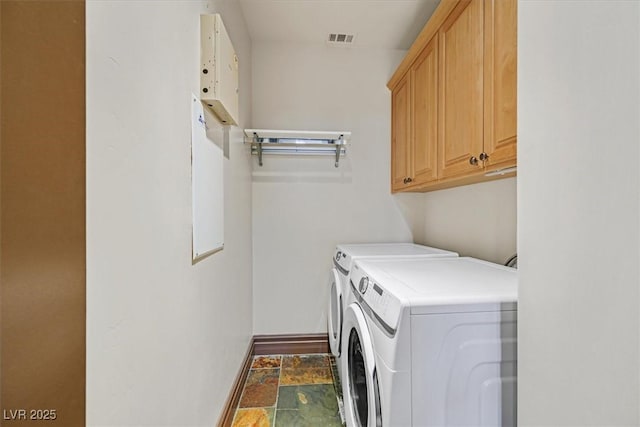 clothes washing area with independent washer and dryer, stone finish flooring, visible vents, baseboards, and cabinet space