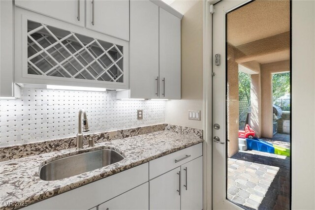 12254 Cape Cortez Ct, Las Vegas, NV 89138 - kitchen with light stone counters, a sink, backsplash, and white cabinetry