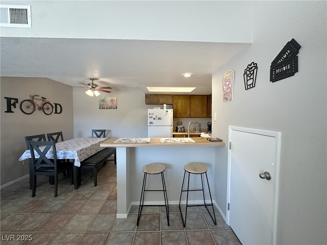 kitchen with a breakfast bar area, brown cabinets, visible vents, freestanding refrigerator, and a peninsula