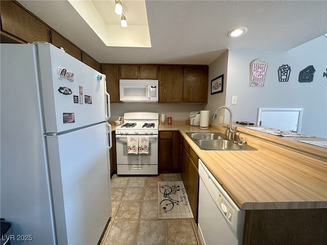 kitchen featuring a sink, white appliances, a peninsula, light countertops, and dark brown cabinets