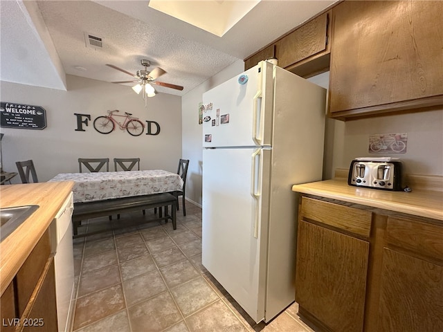 kitchen with brown cabinets, a ceiling fan, visible vents, wooden counters, and freestanding refrigerator