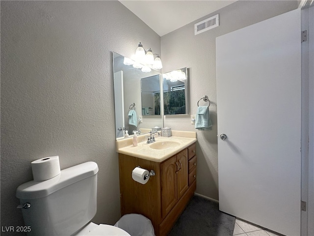 bathroom featuring vanity, tile patterned floors, toilet, visible vents, and a textured wall