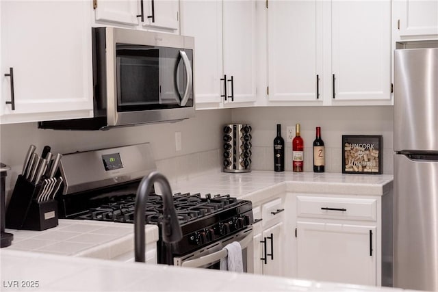 kitchen with tile counters, white cabinetry, and stainless steel appliances