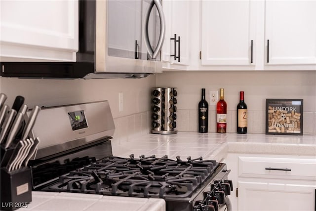 details with tasteful backsplash, stainless steel appliances, white cabinets, and tile countertops