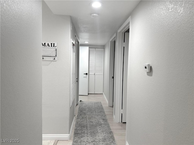 corridor featuring baseboards, light wood-style floors, and a textured wall