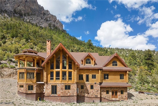 rear view of property with log siding, a chimney, a forest view, and stone siding
