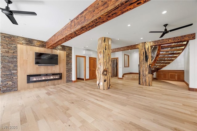unfurnished living room featuring a ceiling fan, wood finished floors, stairs, a glass covered fireplace, and a wall mounted air conditioner