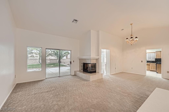 unfurnished living room featuring light colored carpet, baseboards, visible vents, a notable chandelier, and a tile fireplace