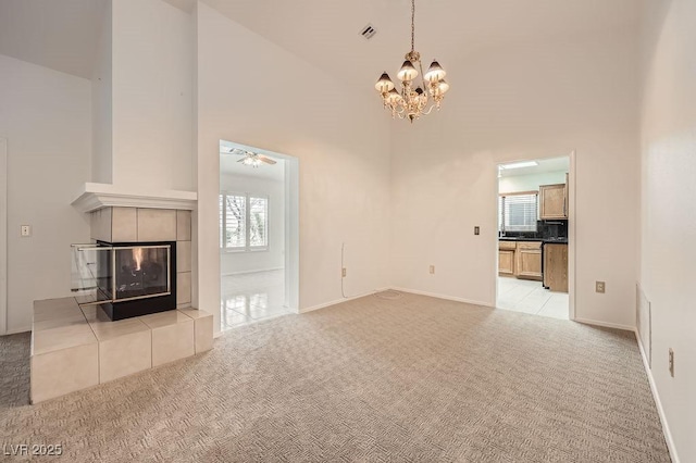 unfurnished living room with an inviting chandelier, light carpet, a towering ceiling, and a tiled fireplace