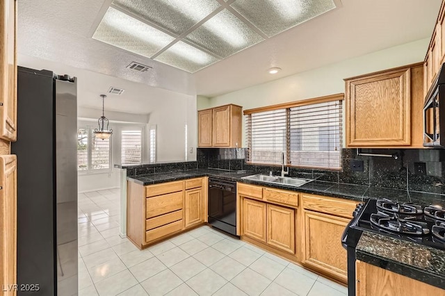 kitchen with a sink, a peninsula, tile countertops, black appliances, and visible vents