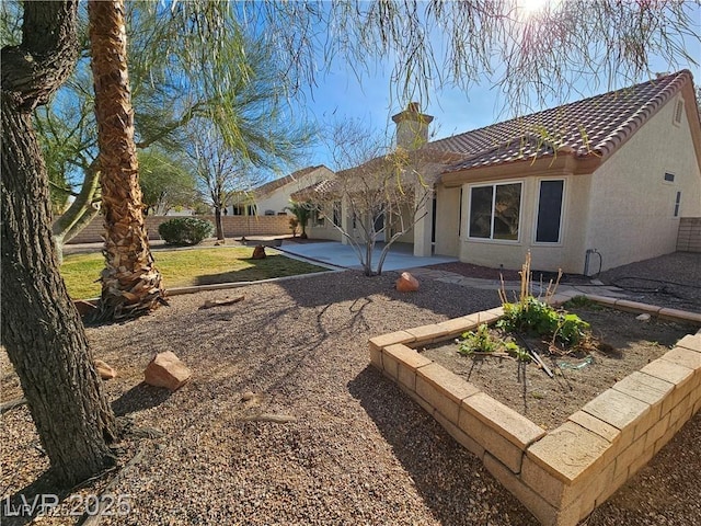 rear view of property with a chimney, a tile roof, a patio area, and stucco siding