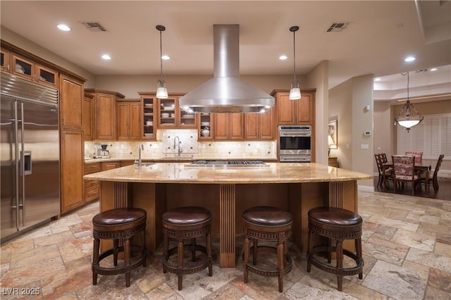 kitchen featuring visible vents, island range hood, brown cabinets, and stainless steel appliances