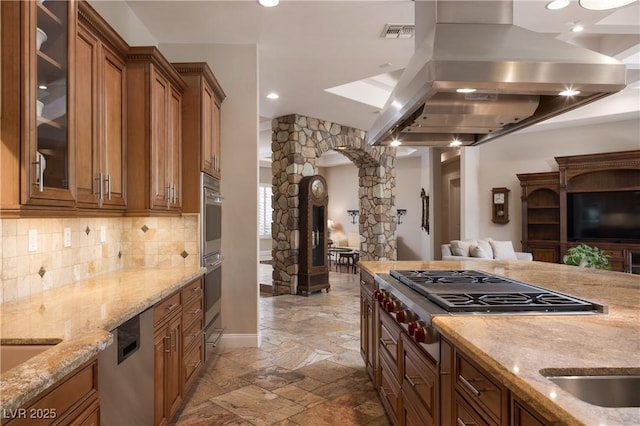 kitchen with arched walkways, brown cabinetry, stone tile flooring, island exhaust hood, and open floor plan