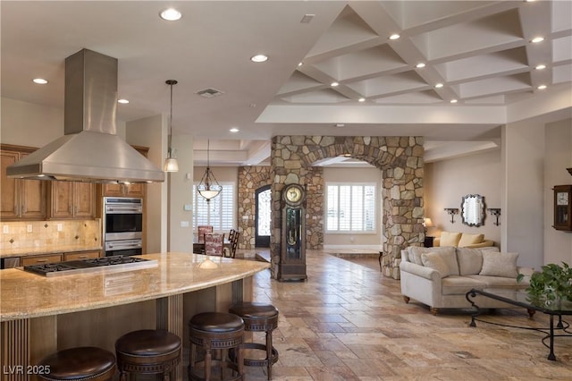 kitchen featuring island range hood, stainless steel appliances, arched walkways, open floor plan, and light stone countertops
