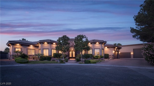 view of front of house with driveway, a tile roof, stucco siding, french doors, and a garage