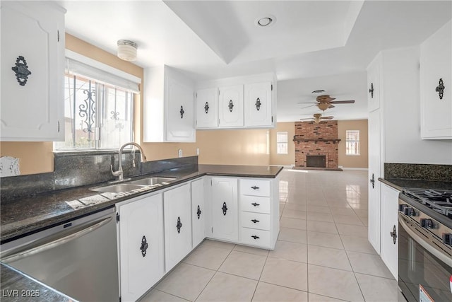 kitchen featuring a ceiling fan, appliances with stainless steel finishes, a fireplace, a sink, and light tile patterned floors