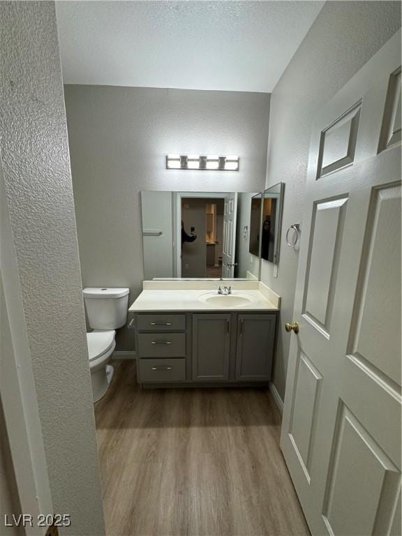 bathroom featuring baseboards, wood finished floors, toilet, and vanity