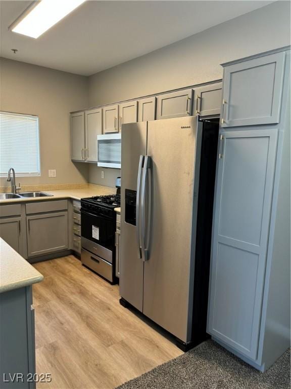 kitchen featuring stainless steel appliances, light wood-style floors, light countertops, a sink, and gray cabinetry