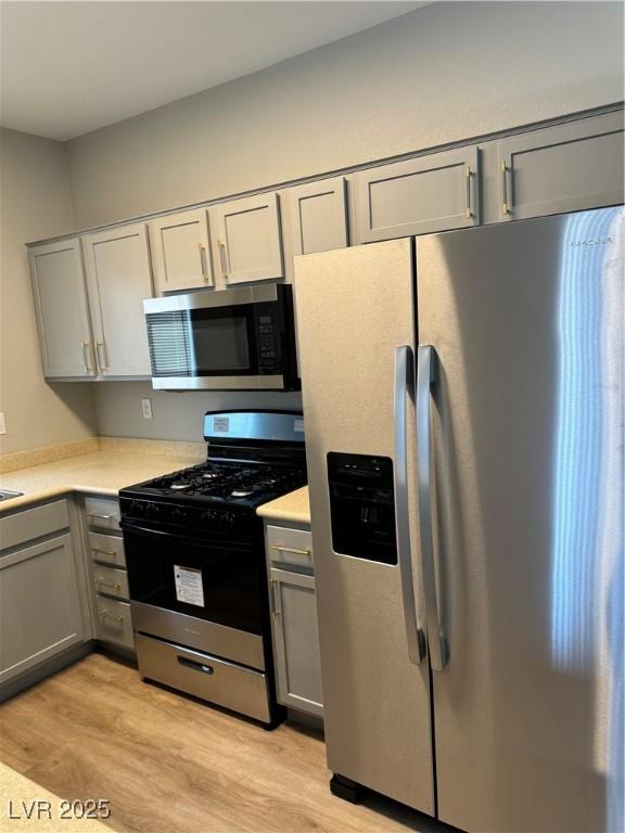 kitchen with appliances with stainless steel finishes, gray cabinetry, light countertops, and light wood finished floors