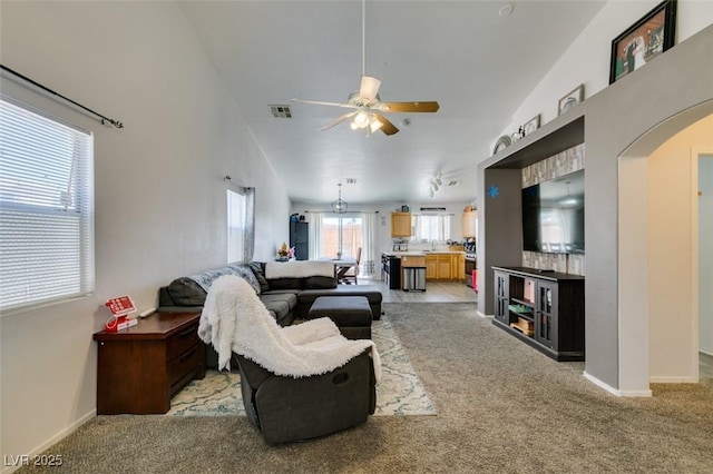 living room with arched walkways, ceiling fan, light carpet, and baseboards